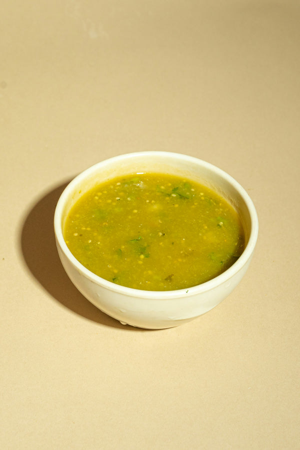 A white bowl of green chile verde — bright Hatch green chile sauce flecked with cilantro.