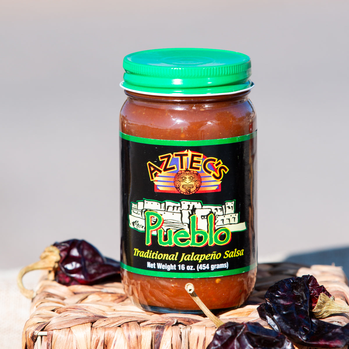 A jar of Salsa Sampler, part of a New Mexican Salsas variety pack, with a green lid and prominently labeled, sits on a wicker surface surrounded by