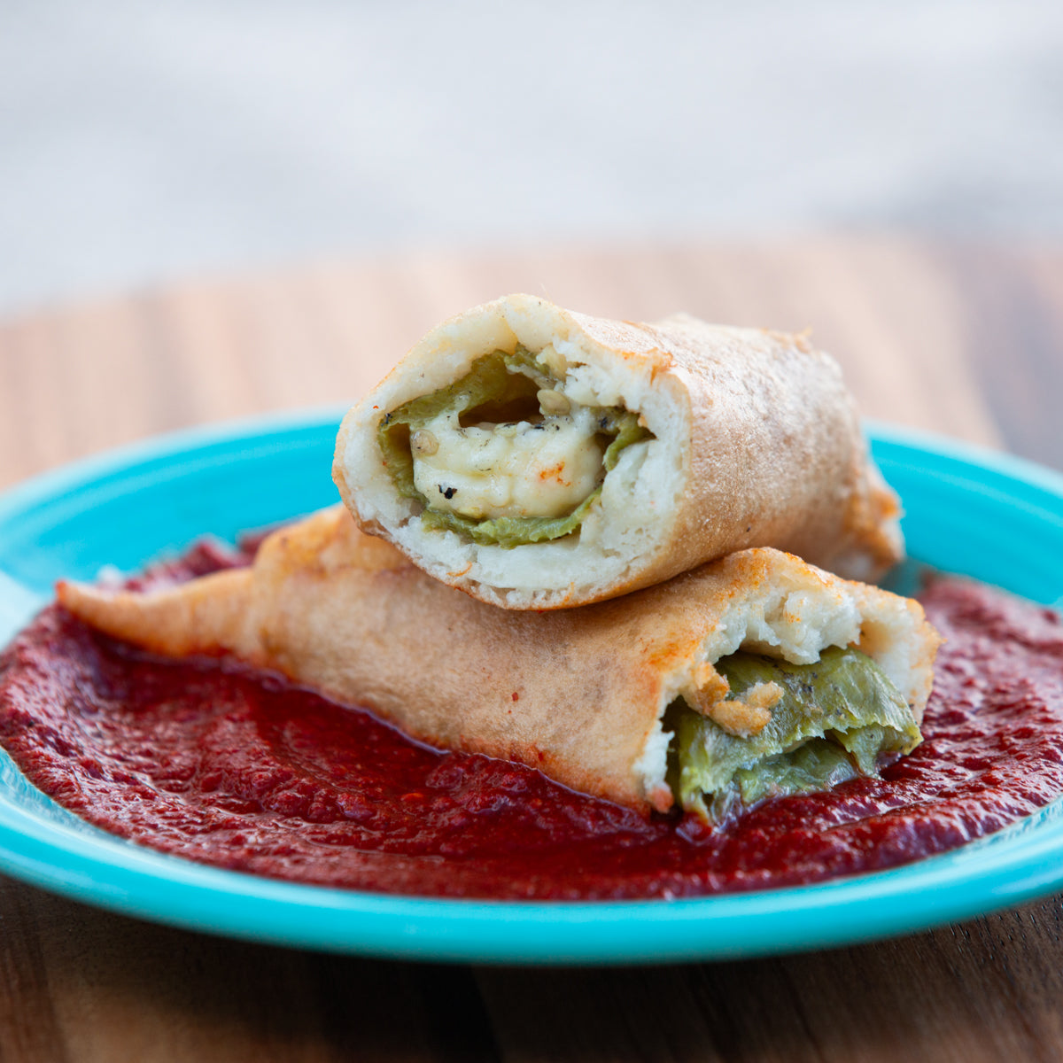 A close-up of a halved breakfast burrito on a blue plate with a red sauce, revealing its filling of scrambled eggs and Hatch Chile Rellenos.