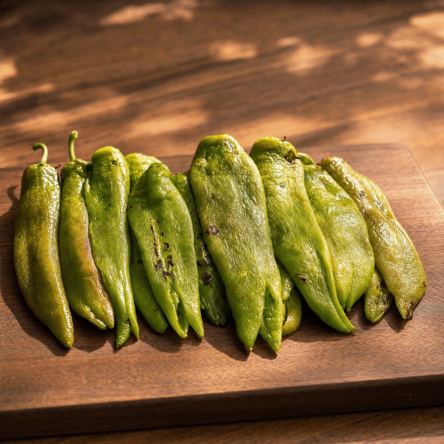 Whole roasted, peeled Hatch green chile pods in a row on a wooden board