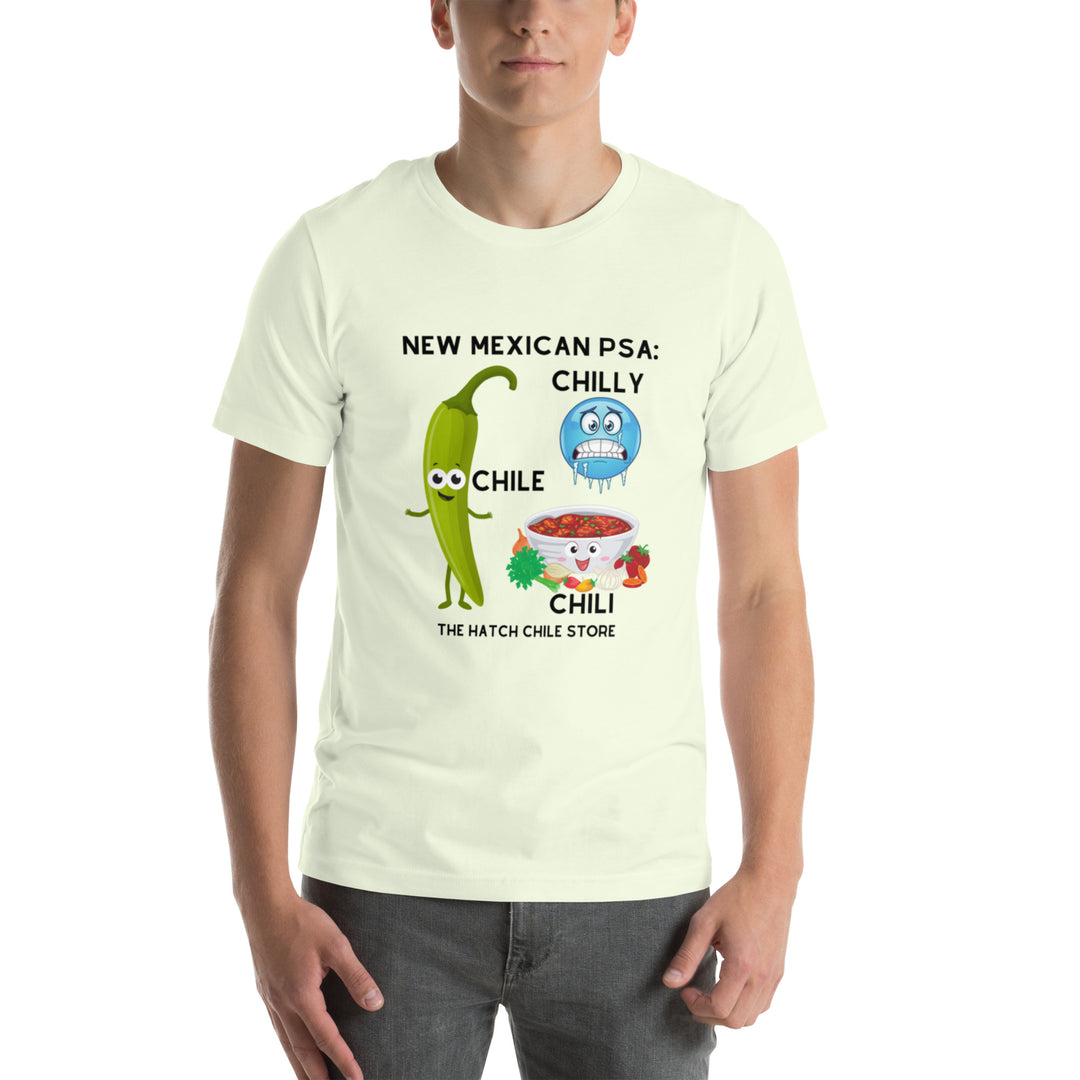 A young man wearing a PSA Shirt in light yellow featuring a humorous design with animated chili peppers and text that reads "new mexican psa: chilly chile - the hatch chili store.
