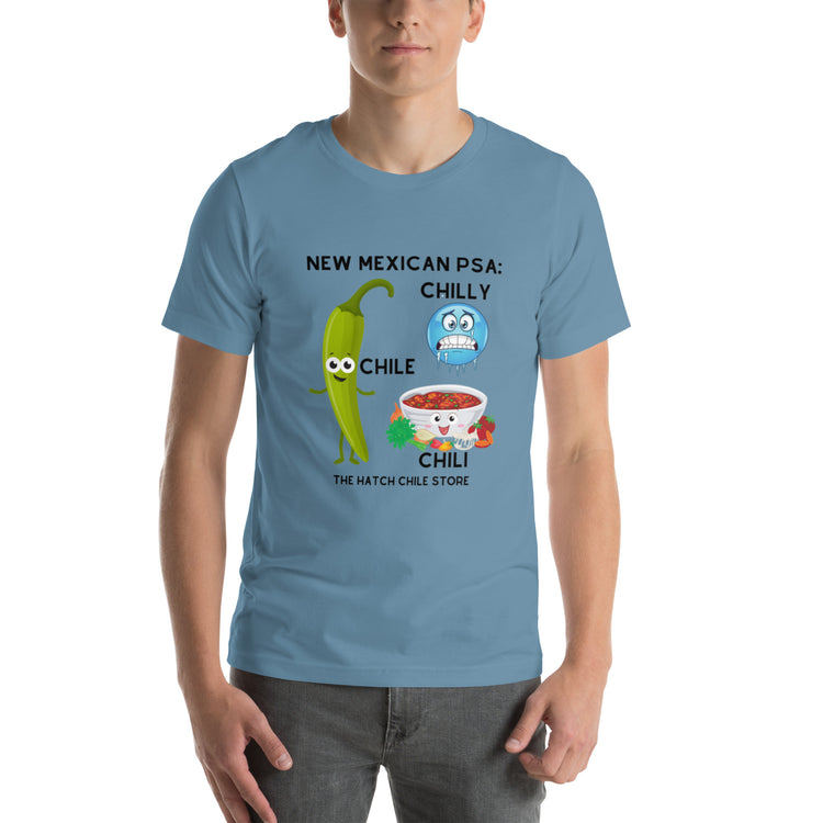 A young man wearing a lightweight, light blue PSA shirt featuring a cartoon of a green chili pepper and a bowl of chili with text "New Mexican PSA: Chilly Chile - The Hatch Chili Store".