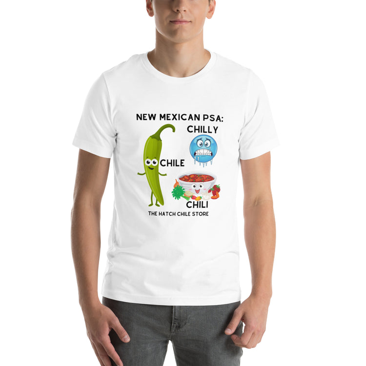 A young man wearing a Chilly Chile - The Hatch Chili Store PSA Shirt featuring a humorous design with cartoon chili peppers and text that reads "New Mexican PSA: Chilly Chile - The Hatch Chili Store.