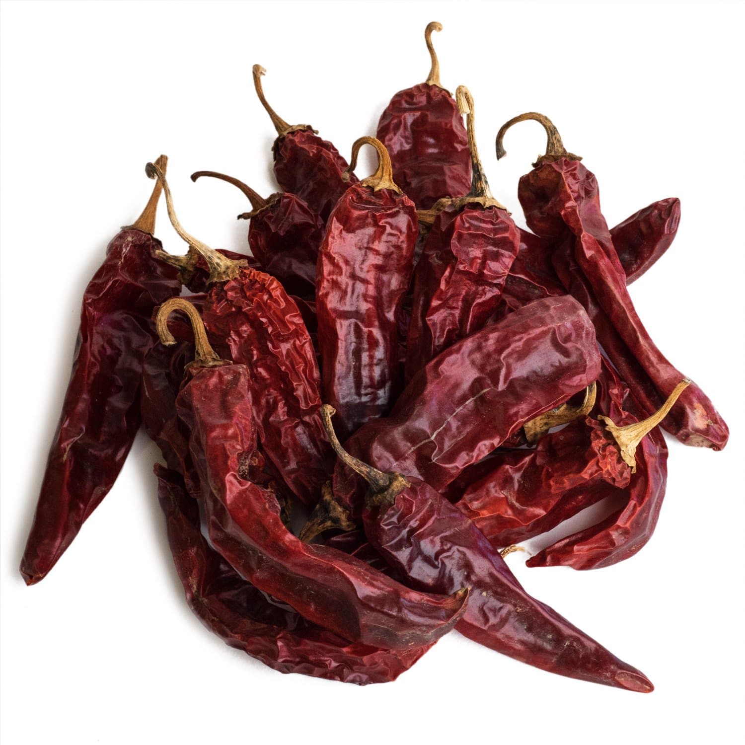 A pile of Dried Hatch Red Chile Pods with wrinkled textures and intact stems, isolated on a white background.