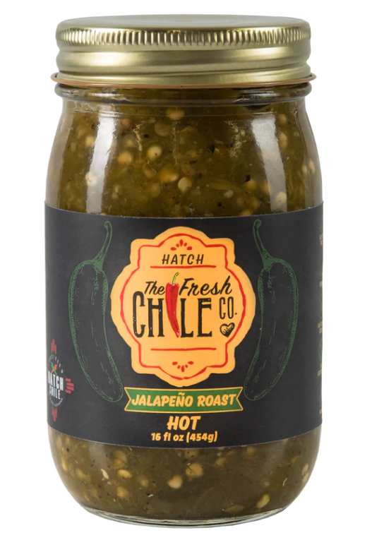 A jar of Hatch Green Jalapeño Roast labeled "hot" with an image of jalapeños on the label. The jar contains green, diced jalapeños and is sealed with