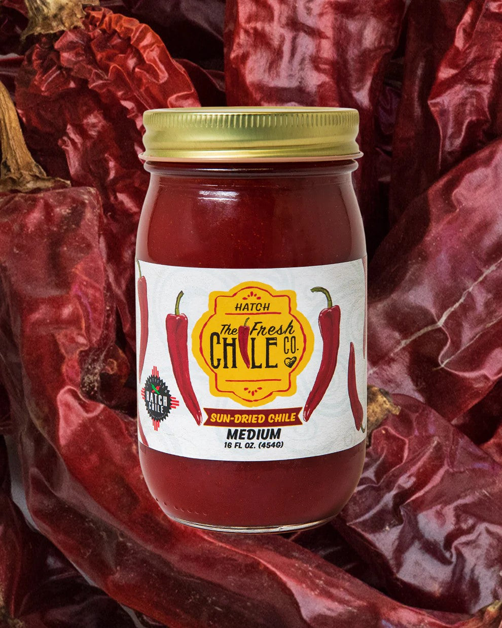 A jar of Sun-Dried Red Chile Sauce labeled as medium heat, centered on a background of whole dried red chiles.