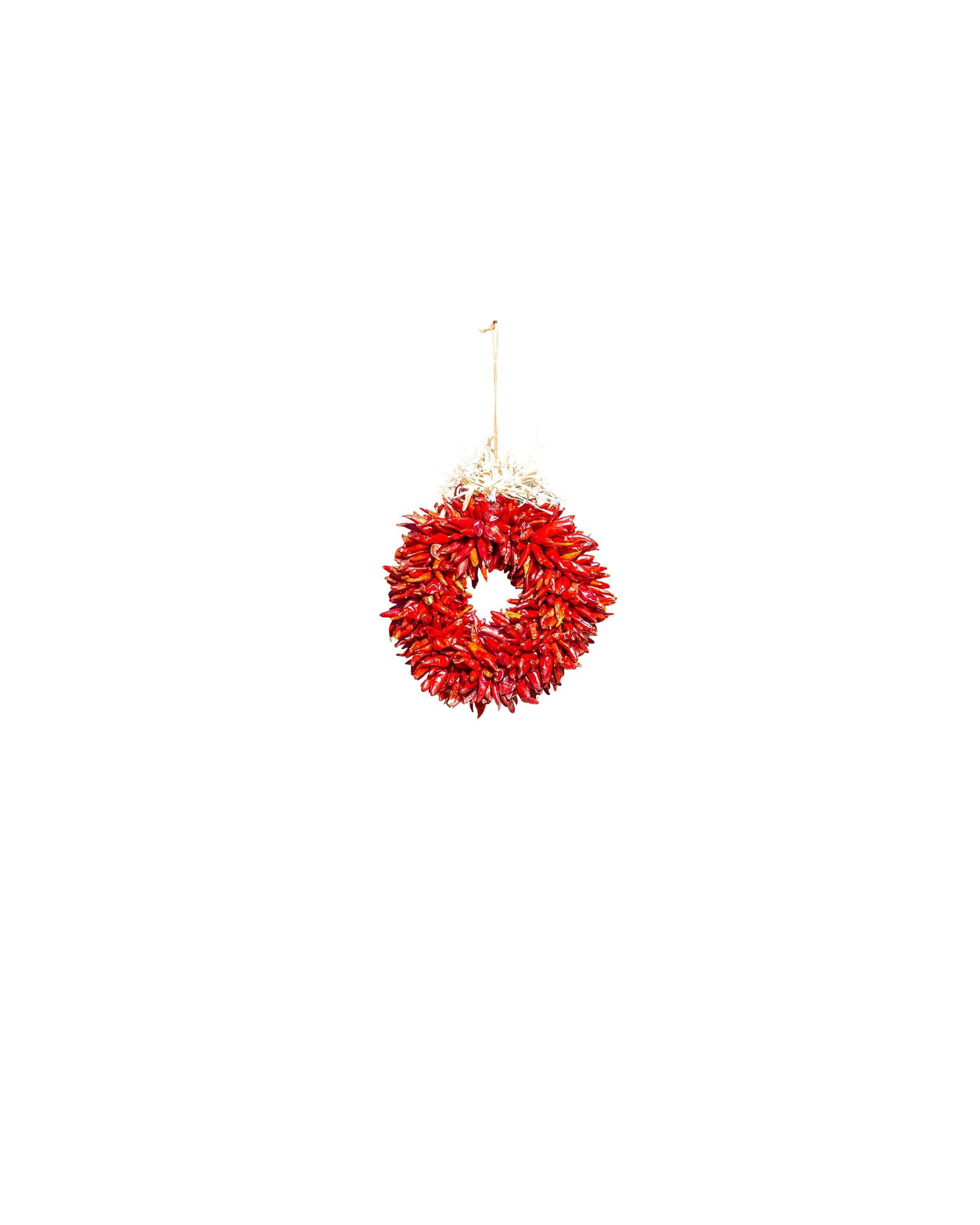A vibrant red Chile Pequin Wreaths hangs against a white background, adding a festive touch with its circular design and natural texture.