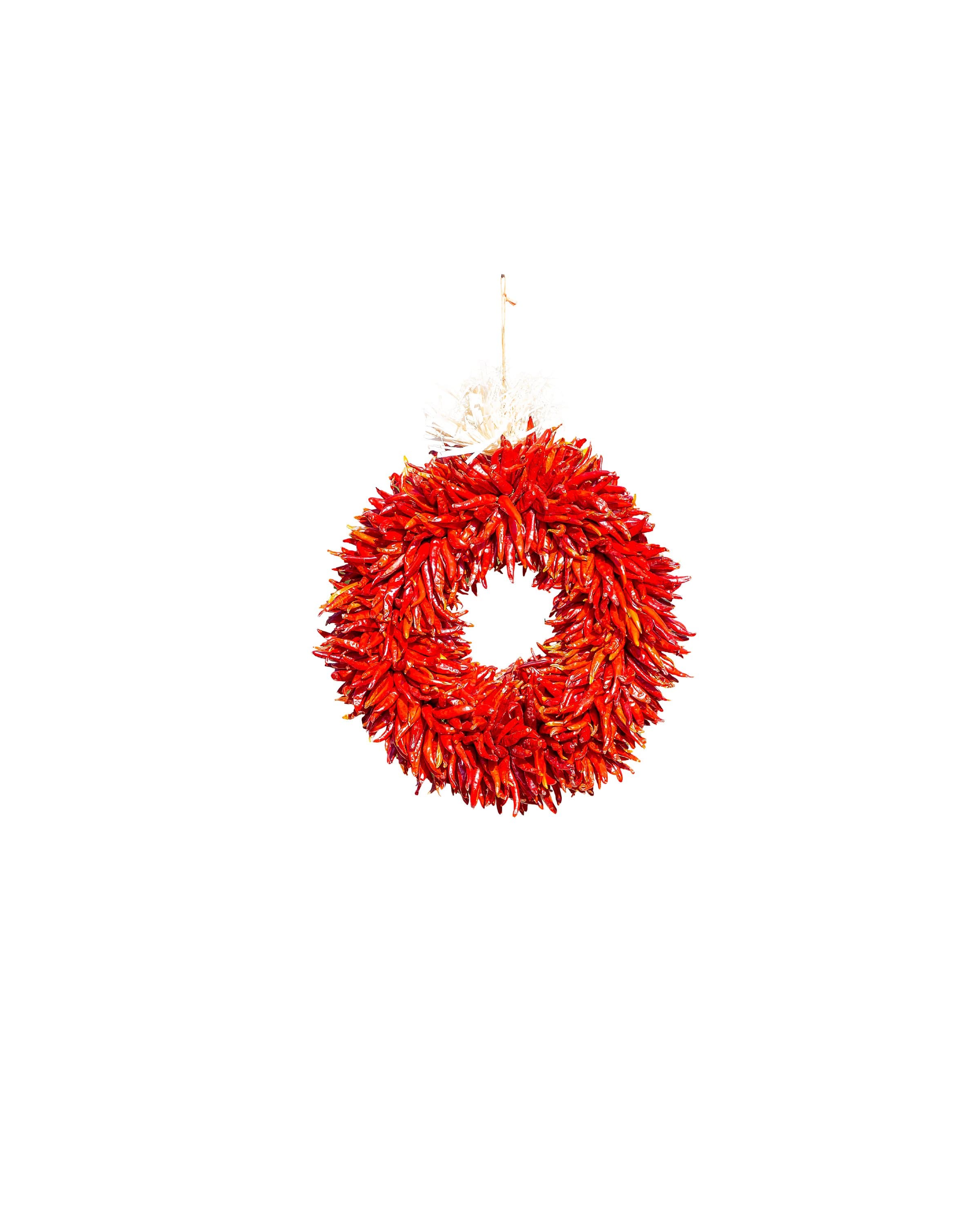 A vibrant red Chile Pequin wreath hangs against a plain white background, adding a fiery decorative touch with the Chile Pequin Wreaths.