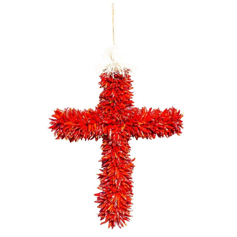 A vibrant red Chile Pequin Cross ristra, hand-made into the shape of a cross, hanging from a twine loop against a stark white background.