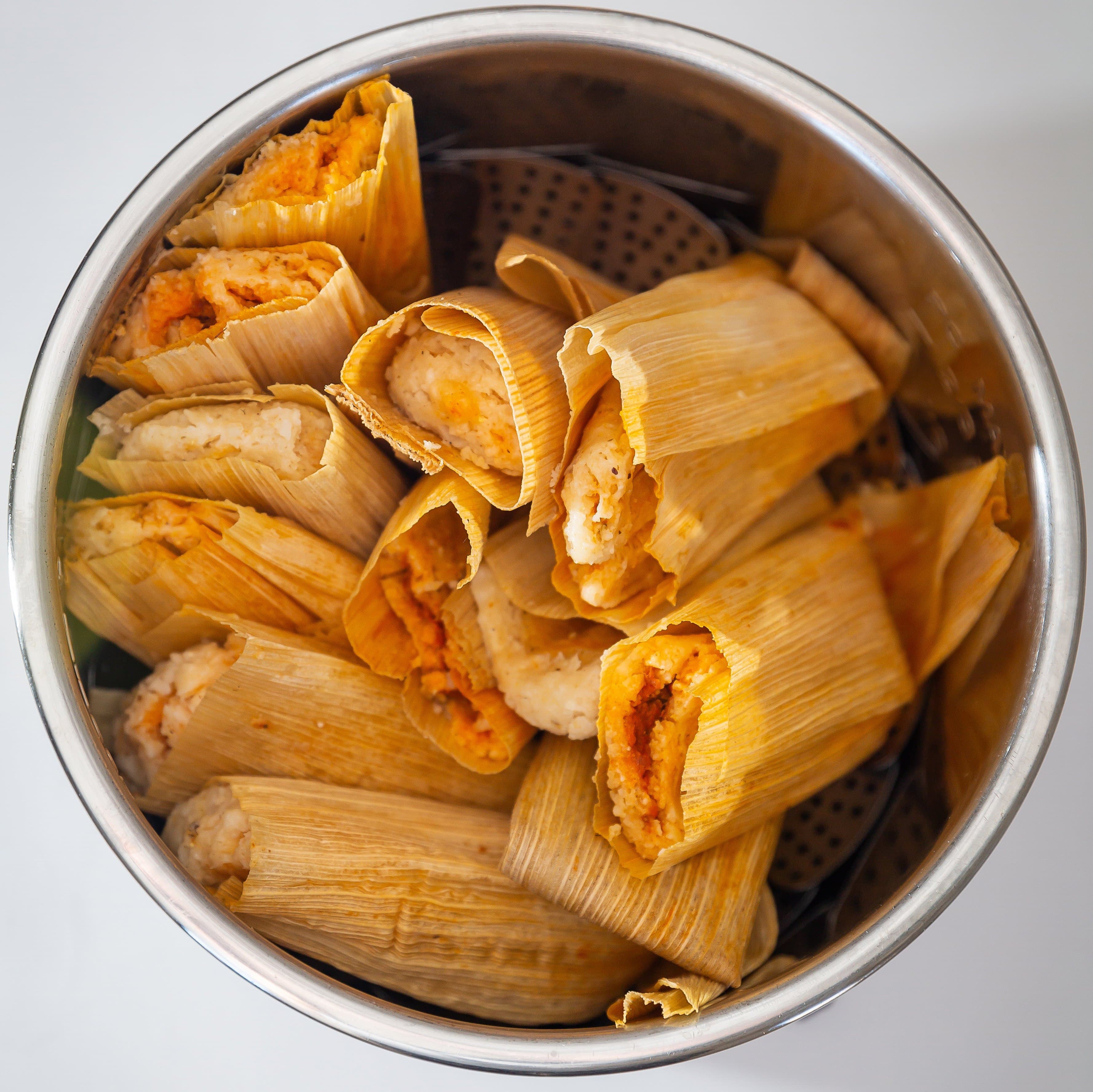 A steamer basket filled with freshly steamed Hatch Red Chile Pork Tamales, some unwrapped at the top revealing the masa and shredded pork filling.