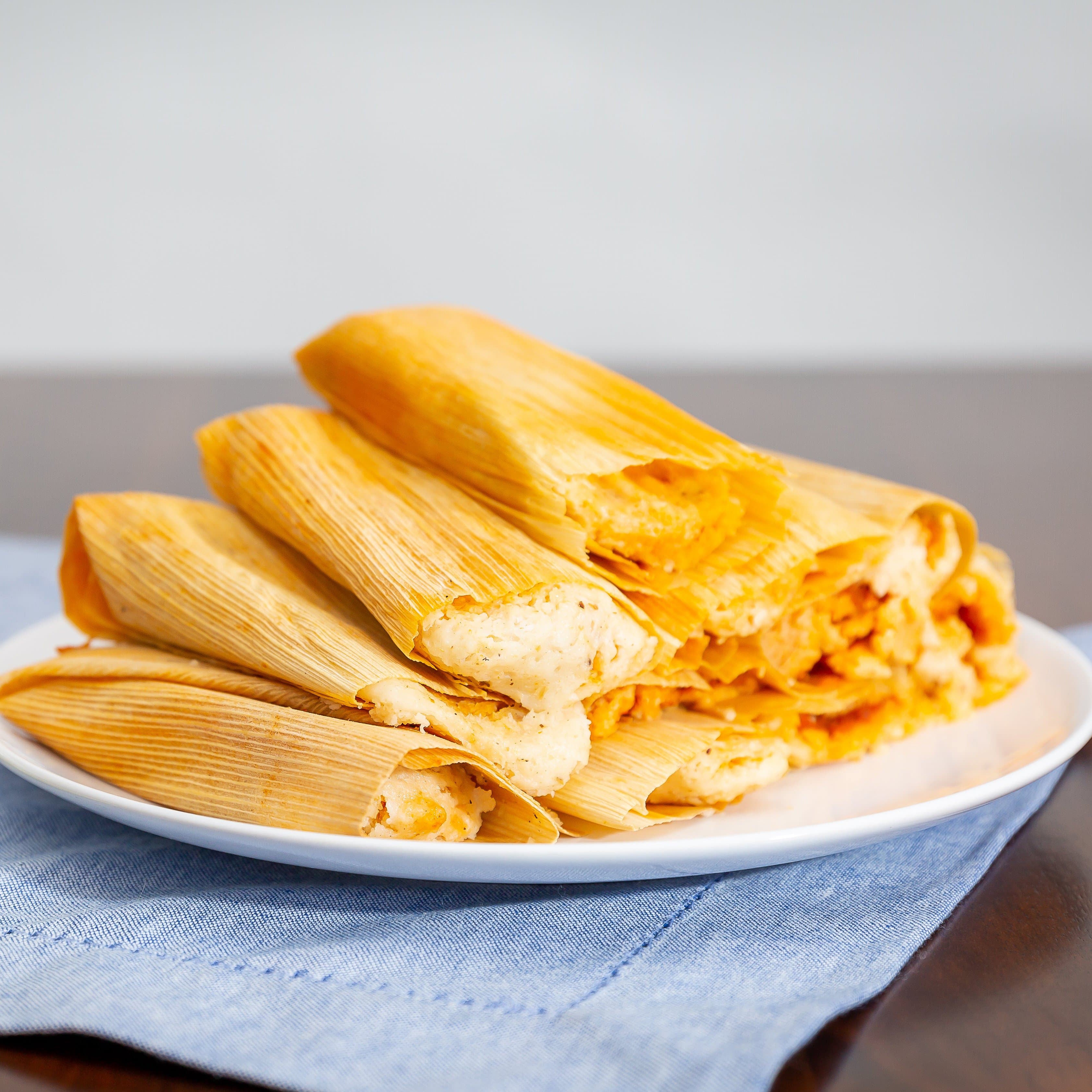 A plate of Hatch Green Chile Cheese Tamales, presented on a white plate resting on a blue cloth on a wooden table.