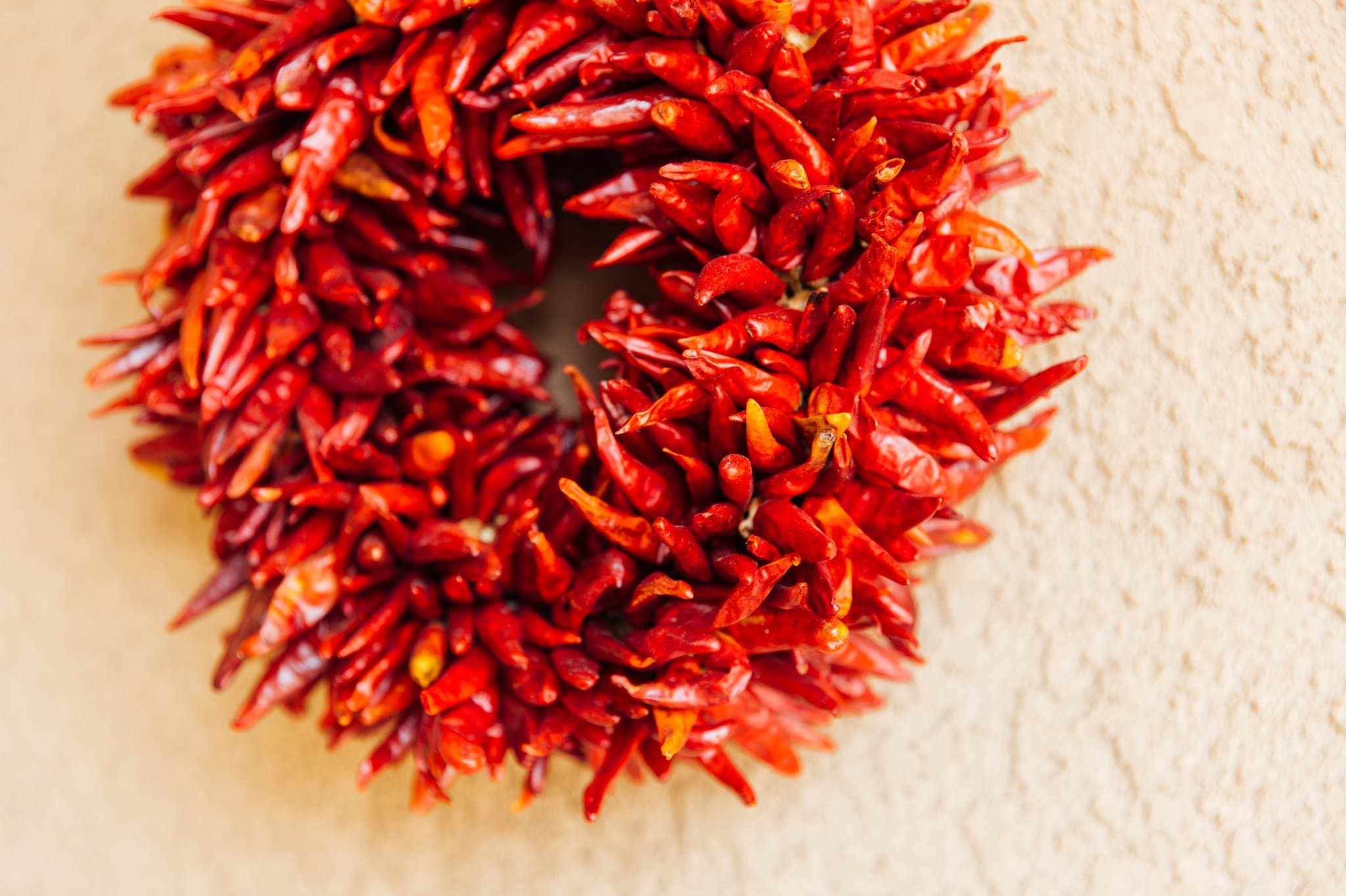A hand-made chile pequin wreath hangs on a textured beige wall, providing a vibrant and spicy decoration.