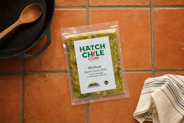 Flat pack of Hatch Chile Store roasted Hatch green chile on a Saltillo tile counter beside a cast-iron skillet