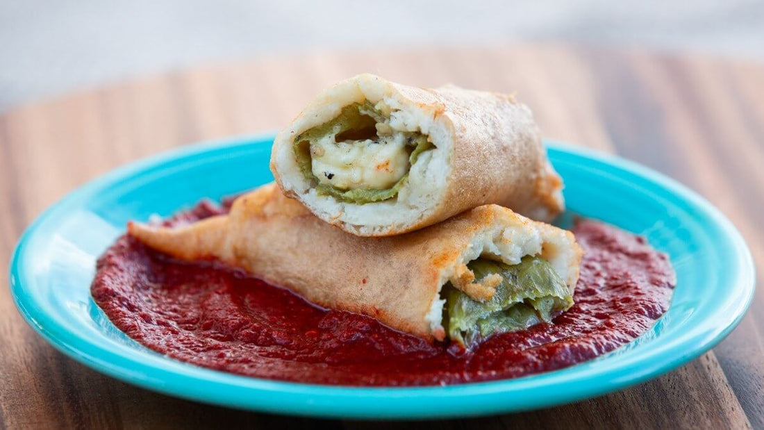 A battered chile relleno cut open to show melted cheese and green chile, stacked on a whole relleno over red chile sauce on a teal plate