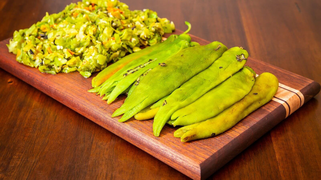 Chopped roasted green chile beside a fanned row of whole roasted green chile pods on a walnut cutting board