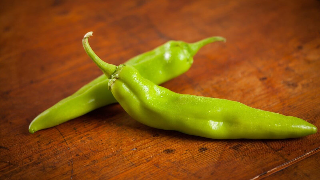 Two fresh green chile pods lying crossed on a dark wooden table