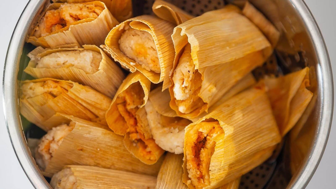 A steamer pot full of cooked red chile tamales in their golden wrappers, several opened to show the masa and red filling