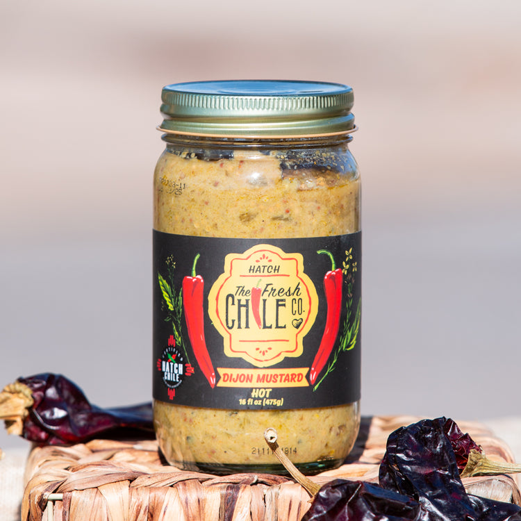 A jar of Ghost Pepper Salsa from the Fresh Chile Co., labeled as hot, set on a wicker mat surrounded by dried chilies, with a blurred background.