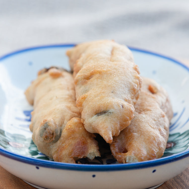 A plate of fried Hatch Chile Rellenos on a ceramic plate with blue patterns, served on a wooden table. The Hatch Chile Rellenos are golden brown with a crispy texture.