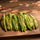 Whole roasted, peeled Hatch green chile pods in a row on a wooden board