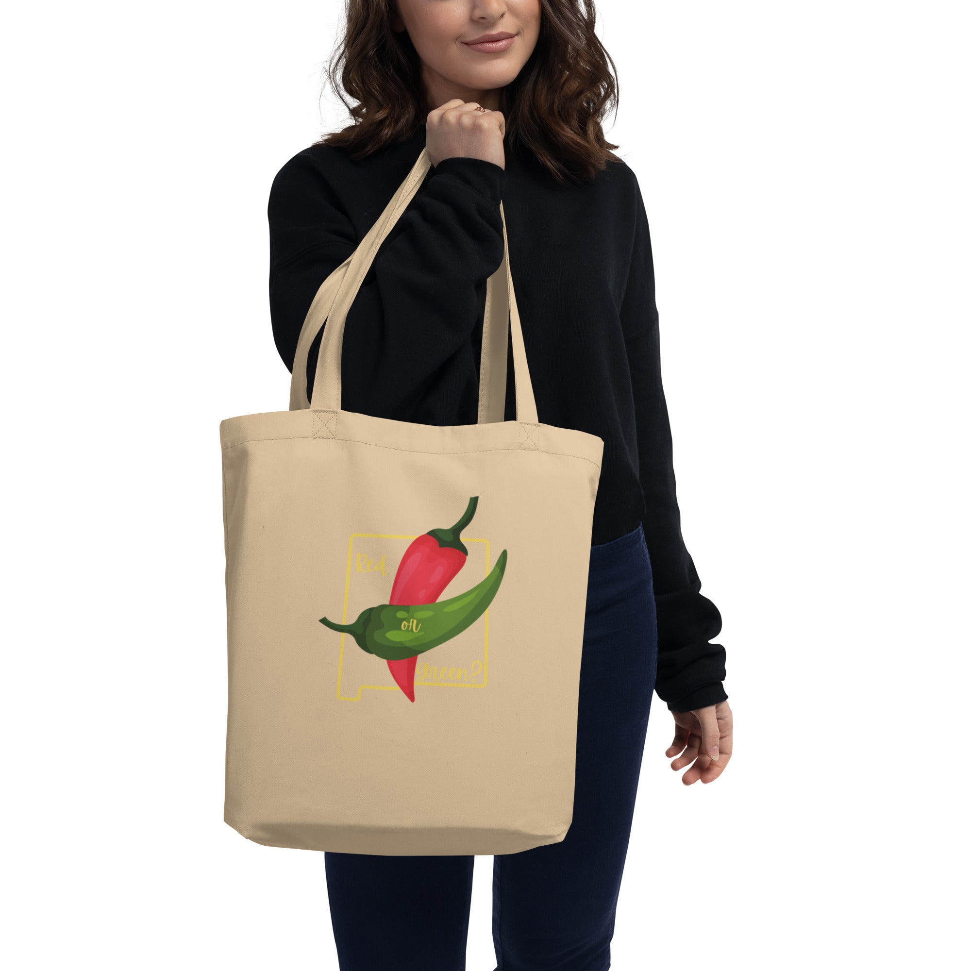 A woman in a black sweater holding a NM State Question Tote Bag with a colorful print of three chili peppers and the phrase "for hot food lovers.