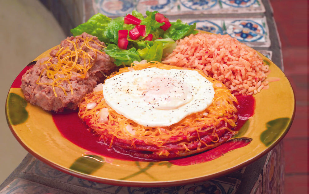 stacked red enchilada topped with a fried egg. refried beans and spanish rice as sides.