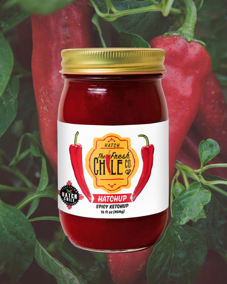 A jar of BBQ Sampler spicy ketchup by The Fresh Chile Co., surrounded by fresh green leaves and red chili peppers, emphasizing its ingredients and flavor profile.