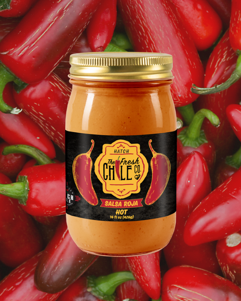 A jar of Hatch Chile Co. Hot Salsa Sampler labeled "hot," surrounded by fresh red peppers. The jar is front and center with a black label featuring illustrations of red peppers.