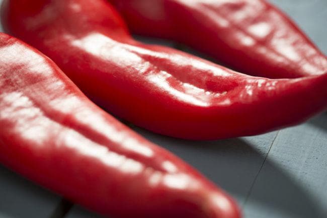 Three bright red chili peppers lying on a textured surface, with a close-up focus emphasizing their glossy and smooth texture, ideal for making Fresh Hatch Red Chile Sauce.