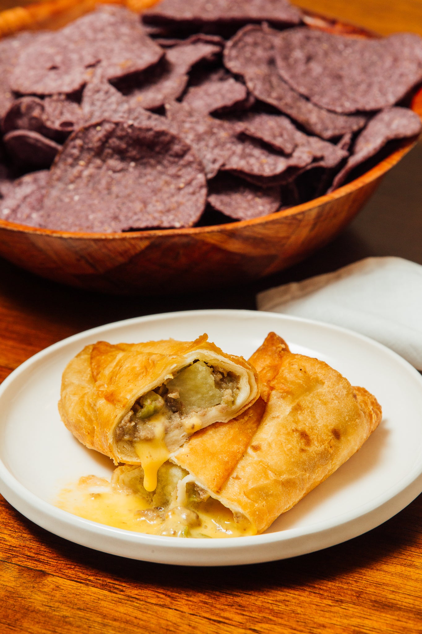 A plate with two Meat Lover Sampler rolls accompanied by a bowl of Hatch Green Chile purple tortilla chips on a wooden table.