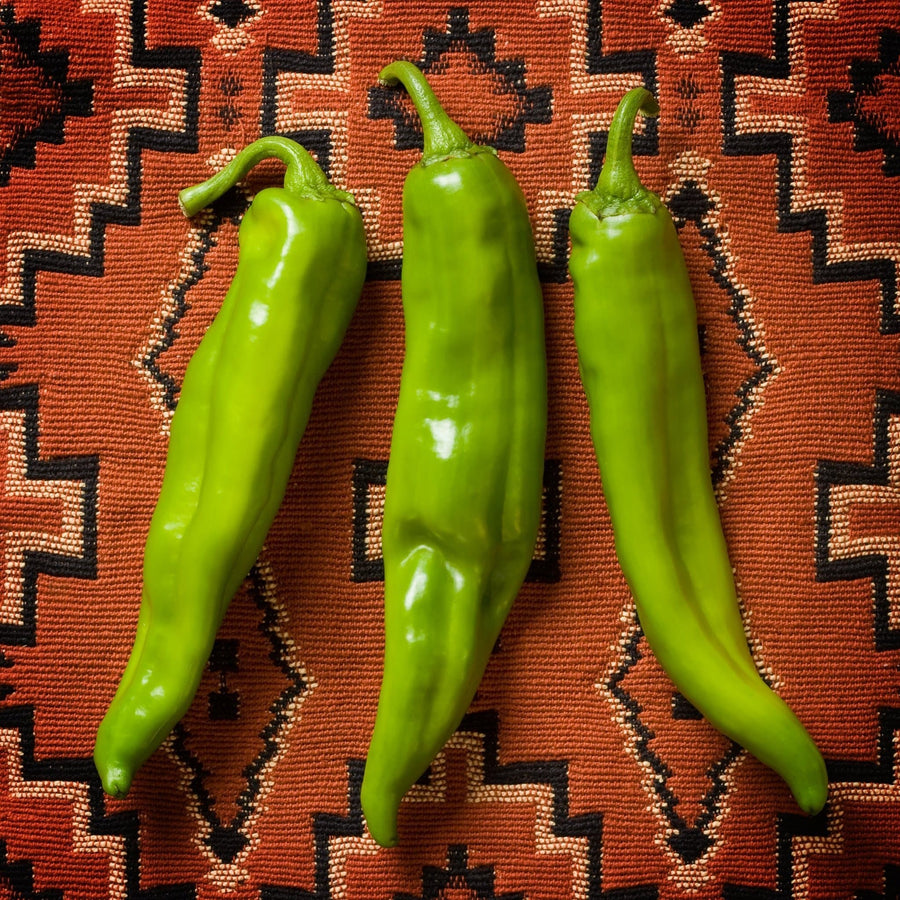 Three fresh Hatch green chile pods on a woven Southwestern blanket