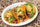 Three tacos made with red chile corn tortillas, filled with seasoned meat, lettuce, tomato and cheese