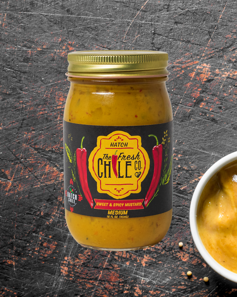 A jar of BBQ Sampler sweet and spicy mustard sits on a dark, textured background. The label shows vibrant red chili peppers and states the product is medium heat. It can be found in our Barbeque Sauces & Mustards section.