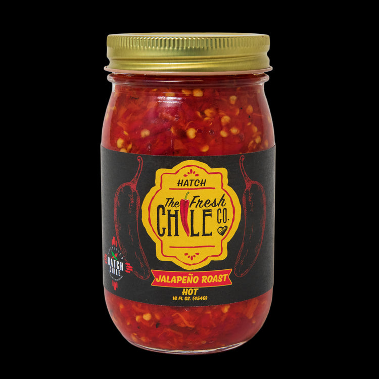 A jar of Hatch Red Jalapeño Roast, labeled as hot, filled with chopped red jalapeños and spices, against a solid black background.