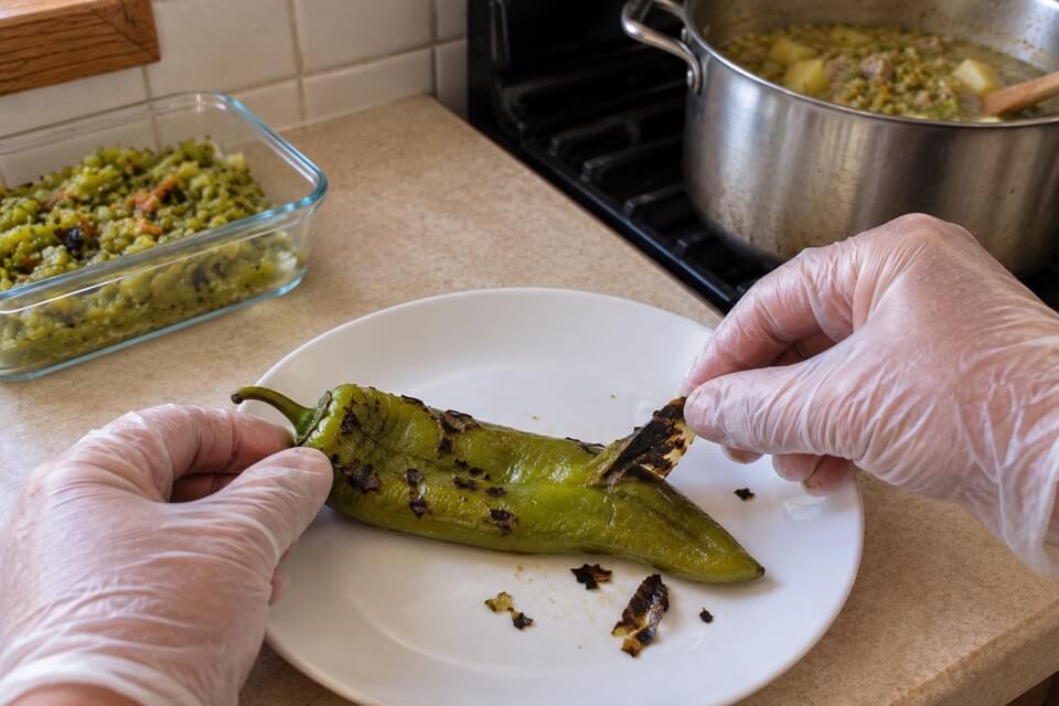 Gloved hands lifting loose, blistered skin from a roasted chile pod